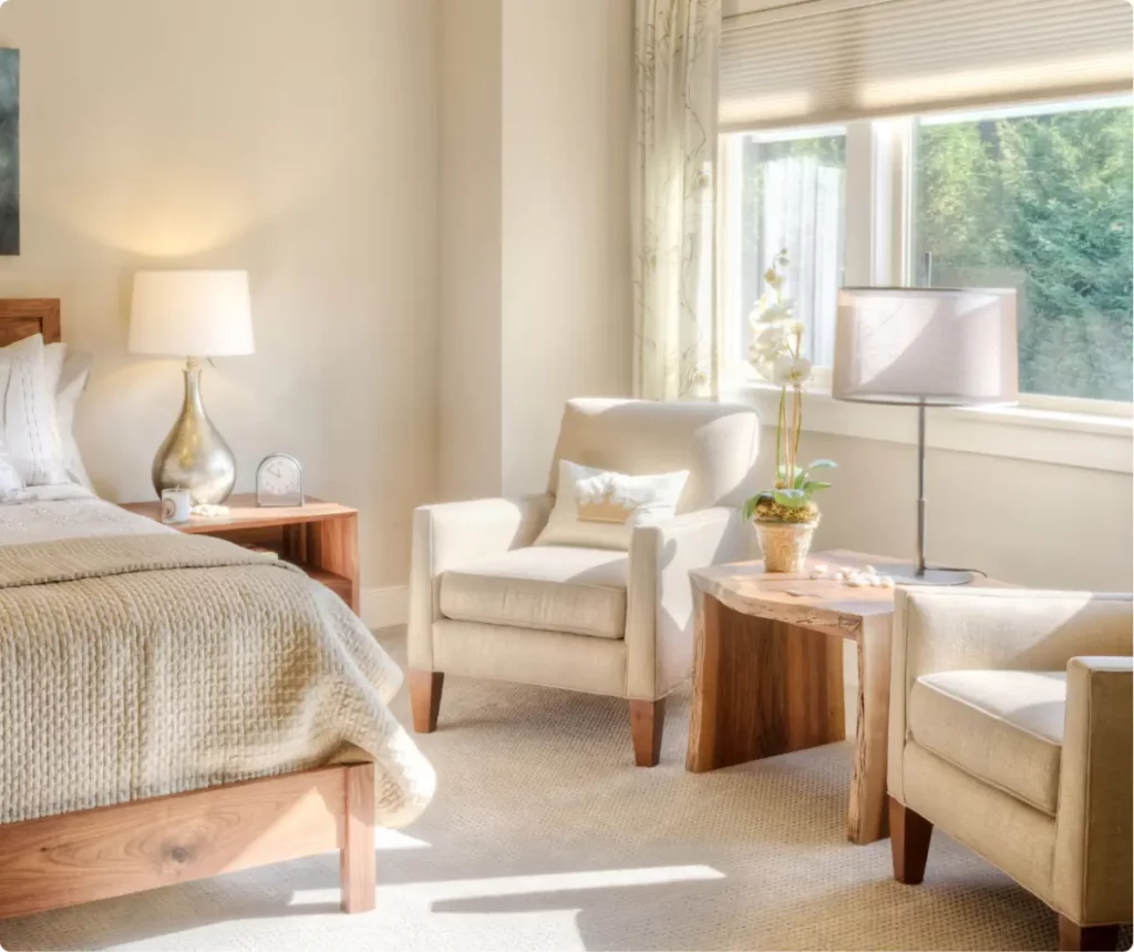Sunlit private bedroom with sitting area, soft neutral decor, and large window, representing luxury detox accommodations.