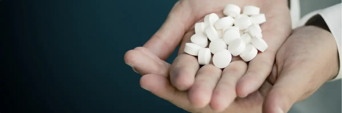 Hands holding a large amount of white prescription pills.
