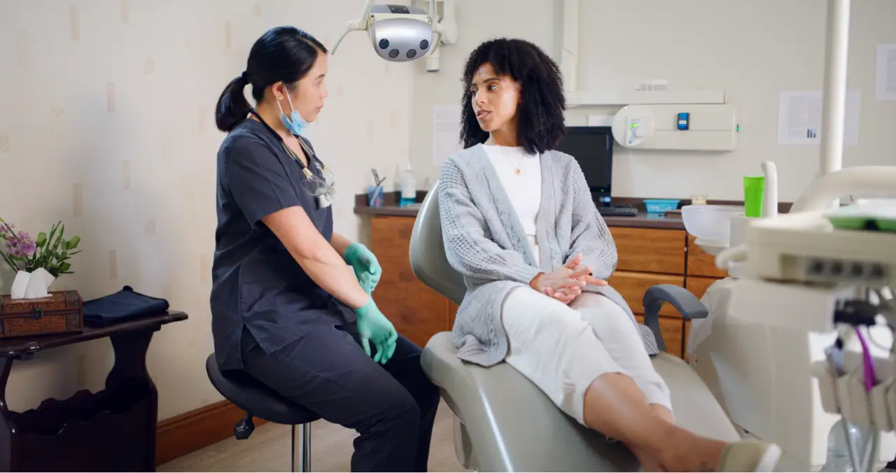 A clinician in scrubs speaking with a female patient in a medical office. This image illustrates the evidence-based psychotherapies for trauma resolution offered within our trauma therapy for artists program.