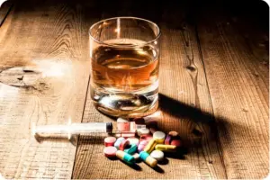Glass of whiskey with prescription pills and syringe on wooden table representing dangers of mixing alcohol and painkillers